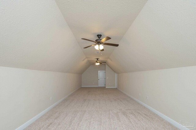 additional living space featuring baseboards, light carpet, vaulted ceiling, and a textured ceiling