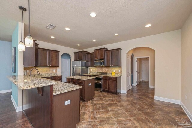 kitchen with arched walkways, appliances with stainless steel finishes, a kitchen island, and a peninsula