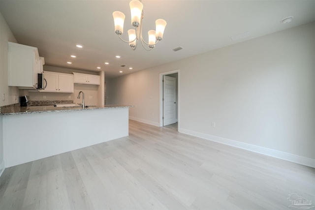 kitchen with light stone counters, range, light hardwood / wood-style flooring, pendant lighting, and white cabinets