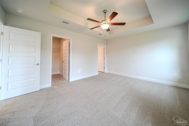 unfurnished bedroom with ceiling fan, a tray ceiling, light carpet, a spacious closet, and a closet