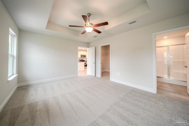 spare room with ceiling fan, light colored carpet, and a tray ceiling