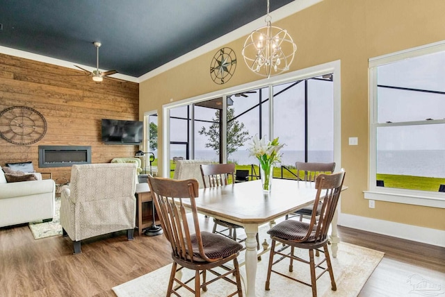 dining area featuring a glass covered fireplace, wood walls, baseboards, and wood finished floors