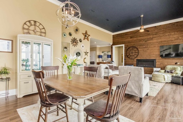 dining space with visible vents, a towering ceiling, ornamental molding, wood finished floors, and ceiling fan with notable chandelier