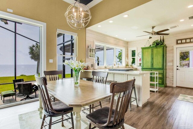 dining area with recessed lighting, ceiling fan with notable chandelier, wooden walls, wood finished floors, and visible vents