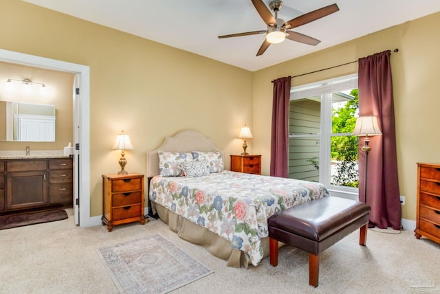 bedroom featuring light colored carpet, ensuite bathroom, ceiling fan, a sink, and baseboards