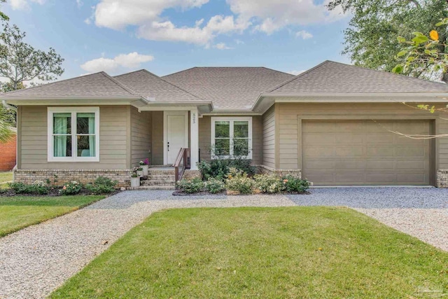 view of front facade with brick siding, roof with shingles, an attached garage, gravel driveway, and a front yard