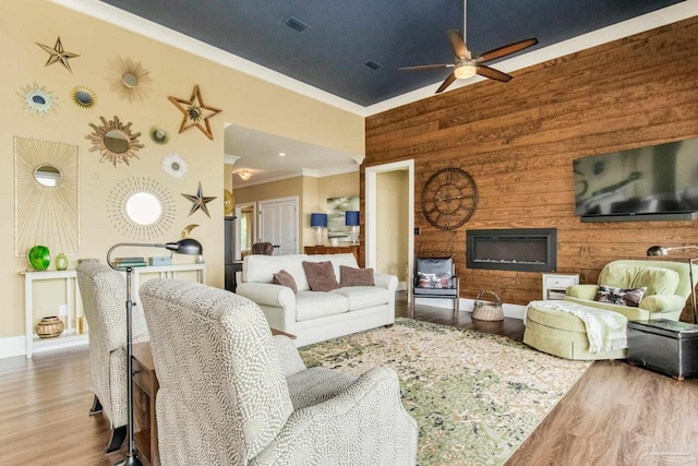 living area with ornamental molding, ceiling fan, a high ceiling, and wood finished floors