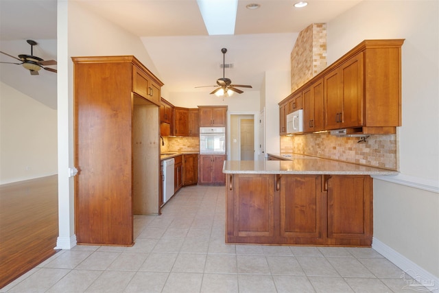 kitchen with white appliances, sink, light tile patterned floors, light stone counters, and kitchen peninsula