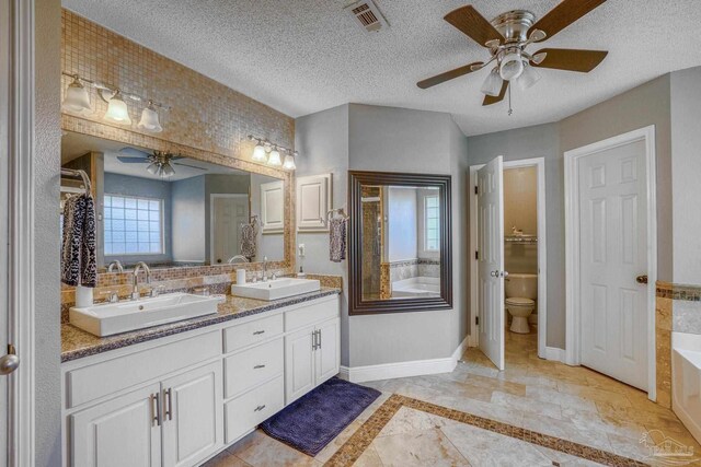 bathroom with a textured ceiling, toilet, a tub to relax in, and vanity