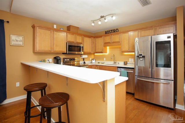 kitchen featuring sink, a kitchen breakfast bar, light brown cabinetry, appliances with stainless steel finishes, and light wood-type flooring