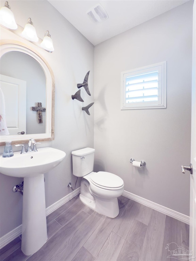 bathroom with visible vents, toilet, a sink, wood finished floors, and baseboards