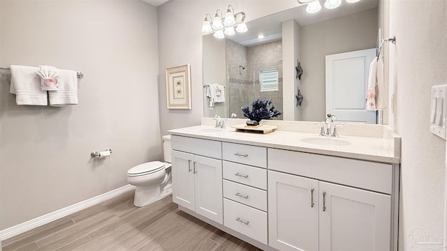 bathroom with baseboards, double vanity, tiled shower, wood finished floors, and a sink