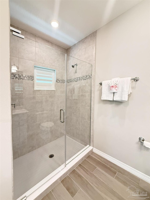 full bath with baseboards, a stall shower, and wood finish floors