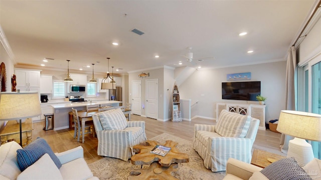 living room with light wood-type flooring, visible vents, ornamental molding, and a ceiling fan