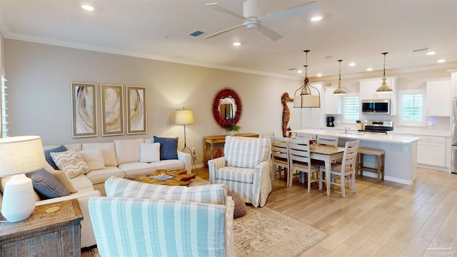 living area featuring visible vents, light wood-style flooring, a ceiling fan, recessed lighting, and crown molding