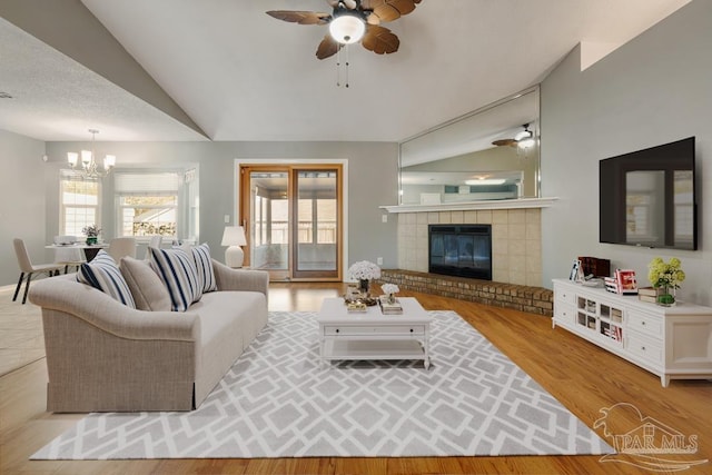 living room featuring ceiling fan with notable chandelier, light wood-type flooring, and vaulted ceiling