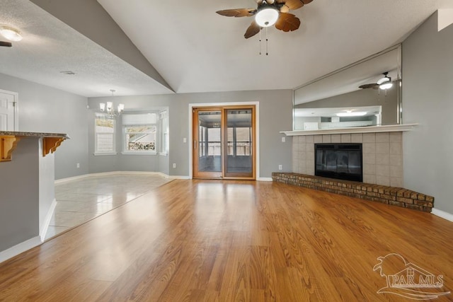 unfurnished living room featuring lofted ceiling, a tile fireplace, ceiling fan with notable chandelier, and light hardwood / wood-style flooring