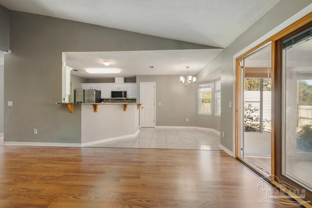 unfurnished living room featuring light hardwood / wood-style flooring, vaulted ceiling, a textured ceiling, and an inviting chandelier