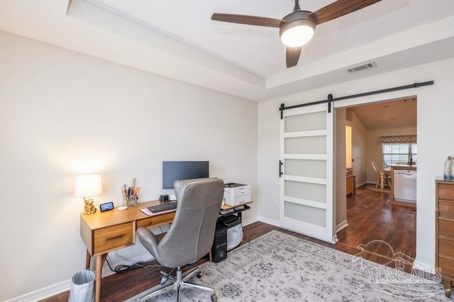 home office with a tray ceiling, dark wood-type flooring, a barn door, and ceiling fan