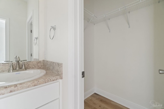 bathroom with a spacious closet, vanity, baseboards, and wood finished floors