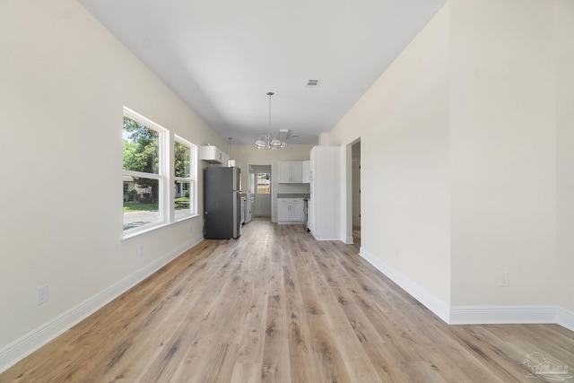 unfurnished living room with a chandelier, light wood-type flooring, visible vents, and baseboards