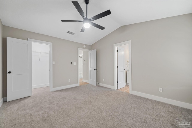 unfurnished bedroom featuring lofted ceiling, ceiling fan, ensuite bathroom, a spacious closet, and light colored carpet