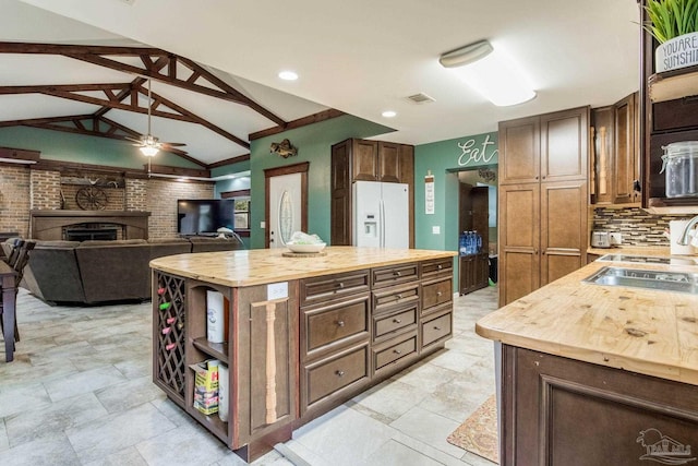 kitchen with white fridge with ice dispenser, lofted ceiling with beams, decorative backsplash, a kitchen island, and butcher block counters