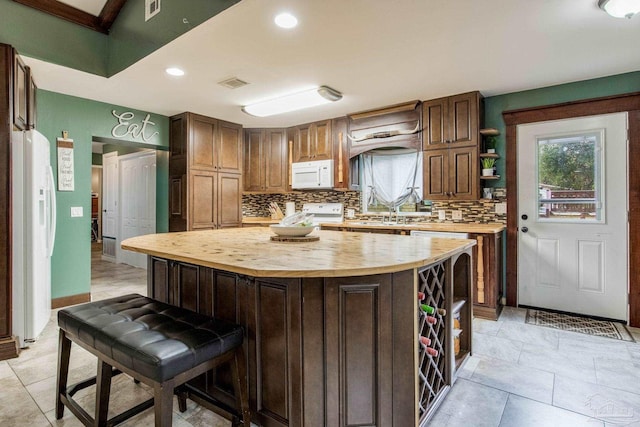 kitchen featuring white appliances, a center island, decorative backsplash, wooden counters, and sink