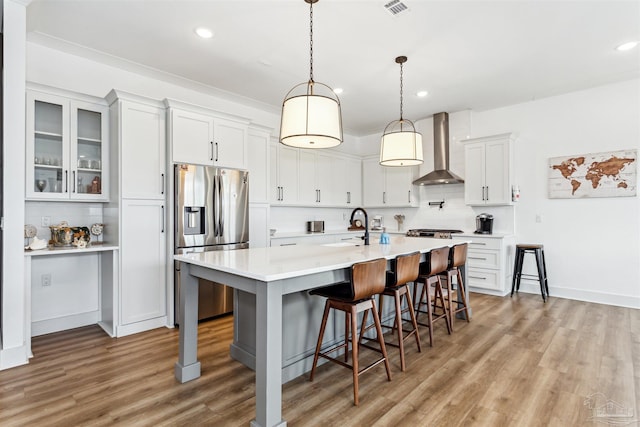 kitchen with wall chimney range hood, decorative backsplash, stainless steel fridge, a kitchen bar, and white cabinetry