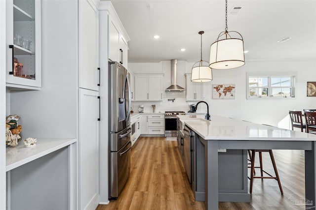 kitchen with white cabinetry, stainless steel appliances, hanging light fixtures, wall chimney range hood, and a kitchen bar