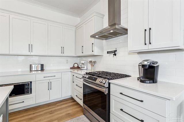 kitchen featuring tasteful backsplash, stainless steel gas range oven, white cabinetry, and wall chimney exhaust hood