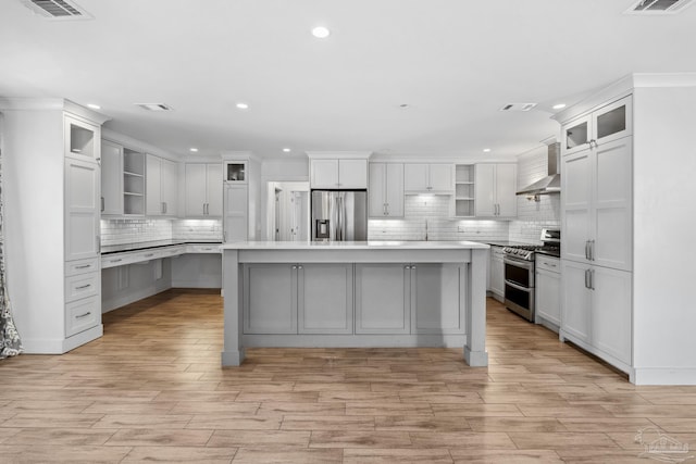 kitchen featuring appliances with stainless steel finishes, wall chimney range hood, decorative backsplash, and a center island