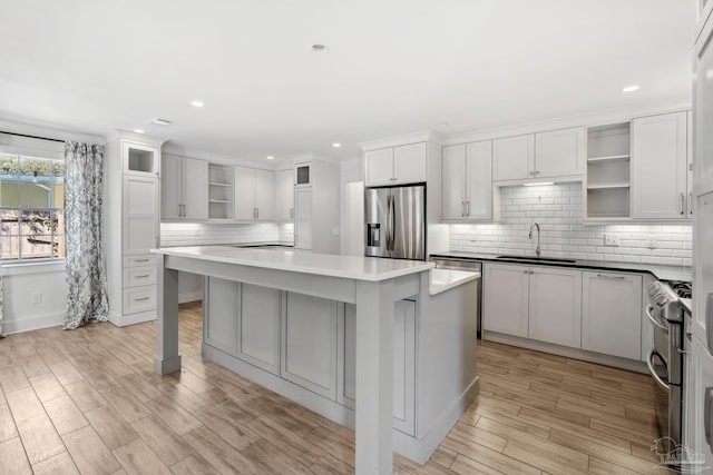 kitchen with sink, white cabinetry, appliances with stainless steel finishes, a center island, and light wood-type flooring