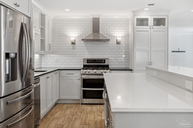 kitchen featuring appliances with stainless steel finishes, wall chimney exhaust hood, white cabinetry, and light hardwood / wood-style floors