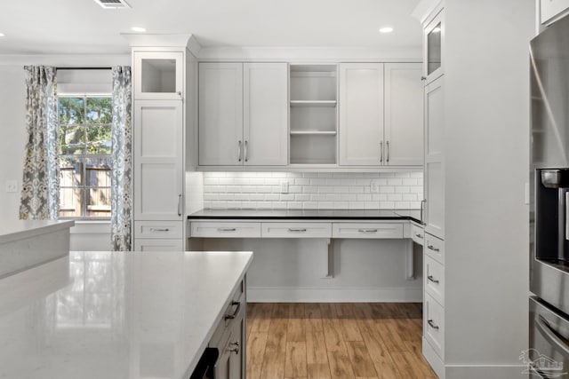 kitchen featuring backsplash, dark stone counters, white cabinetry, stainless steel appliances, and light wood-type flooring