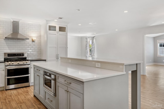 kitchen featuring wall chimney exhaust hood, a kitchen island, stainless steel range oven, and light wood-type flooring