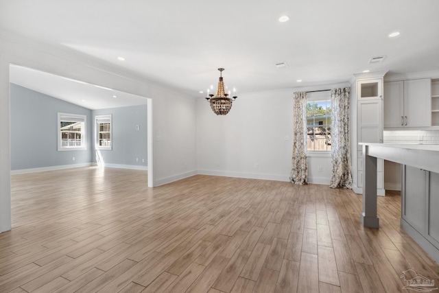 interior space with ornamental molding, vaulted ceiling, an inviting chandelier, and light wood-type flooring