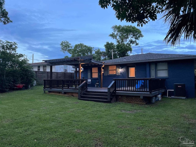 back house at dusk with central AC unit, a pergola, a wooden deck, and a lawn