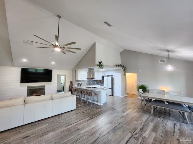 living room with light wood-type flooring, high vaulted ceiling, and ceiling fan