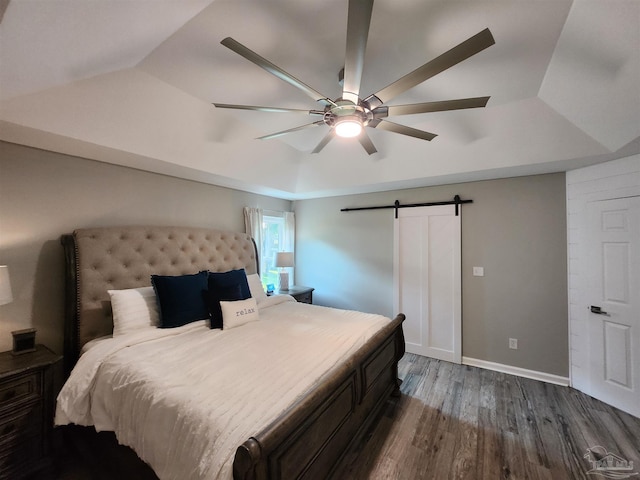 bedroom featuring a raised ceiling, a barn door, ceiling fan, and dark hardwood / wood-style floors