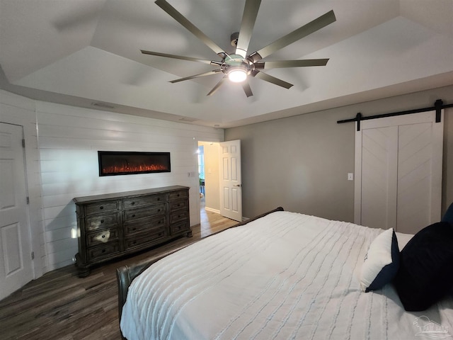 bedroom with ceiling fan, wooden walls, dark wood-type flooring, a barn door, and lofted ceiling