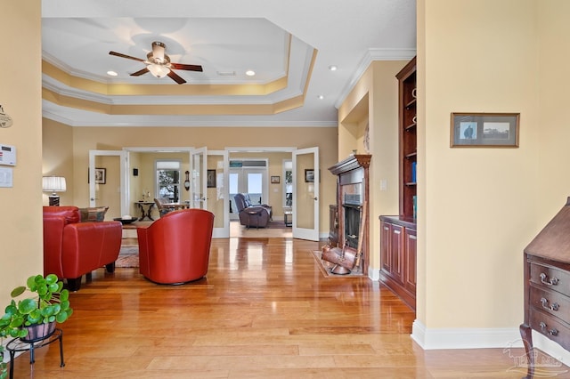 living room featuring ceiling fan, a tray ceiling, light hardwood / wood-style flooring, ornamental molding, and built in shelves