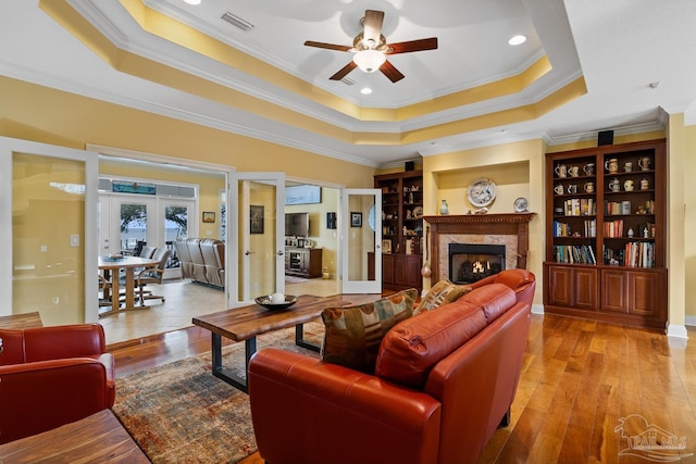 living room with a tray ceiling, ornamental molding, built in features, french doors, and a high end fireplace