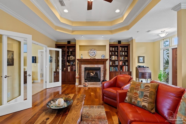 living room featuring hardwood / wood-style floors, a raised ceiling, a premium fireplace, ornamental molding, and french doors