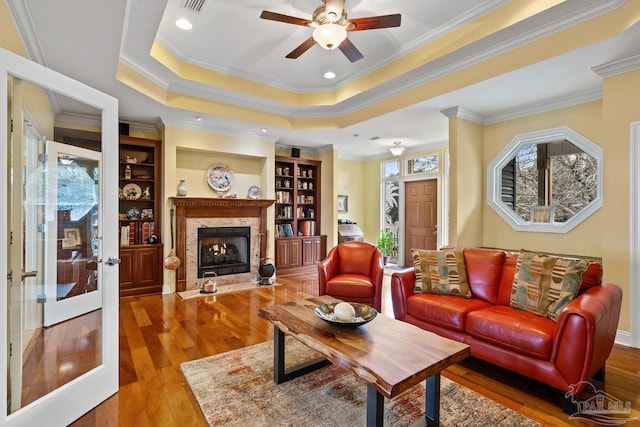 living room featuring wood-type flooring, a premium fireplace, a tray ceiling, and ornamental molding