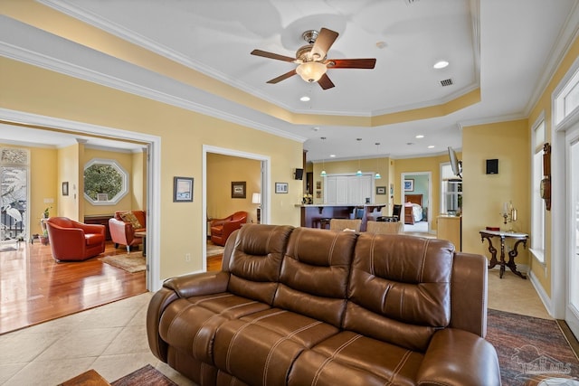 tiled living room featuring ceiling fan, ornamental molding, and a tray ceiling