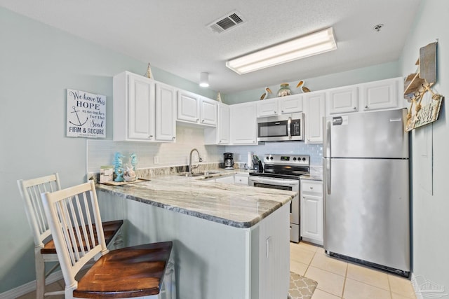 kitchen with white cabinets, appliances with stainless steel finishes, sink, kitchen peninsula, and light stone counters