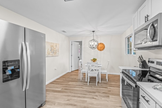 kitchen featuring appliances with stainless steel finishes, decorative light fixtures, an inviting chandelier, white cabinets, and light hardwood / wood-style floors