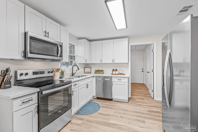 kitchen with appliances with stainless steel finishes, light hardwood / wood-style flooring, white cabinetry, and sink