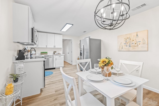 dining area with sink, light hardwood / wood-style flooring, and an inviting chandelier